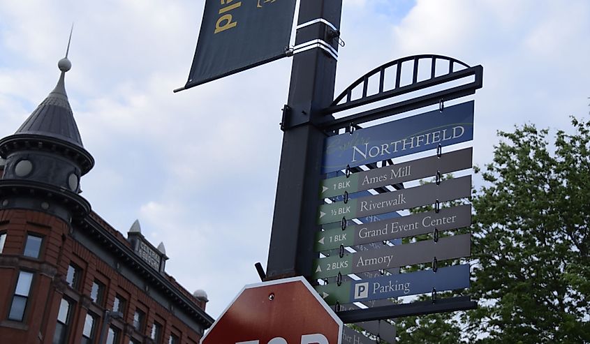 Street post showing directions and partial stop sign with domed building in background on a blue sky with white clouds, Northfield,Minnesota