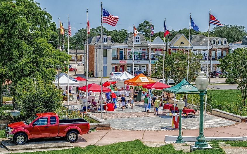 Weekly Crescent City Farmers Market is held at LaSalle's Landing at William's Blvd. and the Mississippi River. Tents, flags, shoppers, vendors complete the image.
