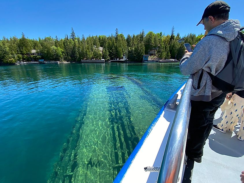 A man aboard a boat taking a picture of a sunken ship in a shallow harbour