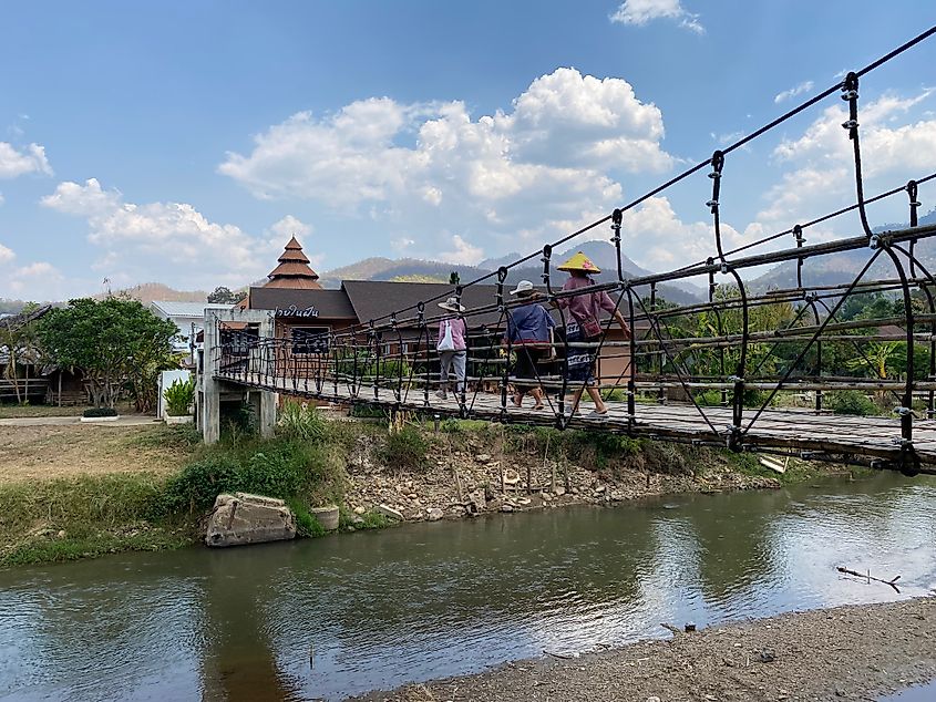 Three female Thai farmers crossing a bamboo bridge over a modest river.
