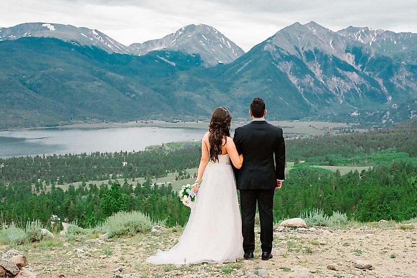 Bride and groom facing toward the rocky mountains and mountain lake. Summer wedding in Colorado.