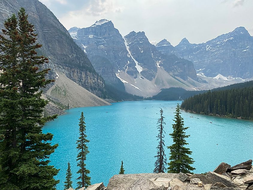 A bright blue lake surrounded by mountains with light snow cover.