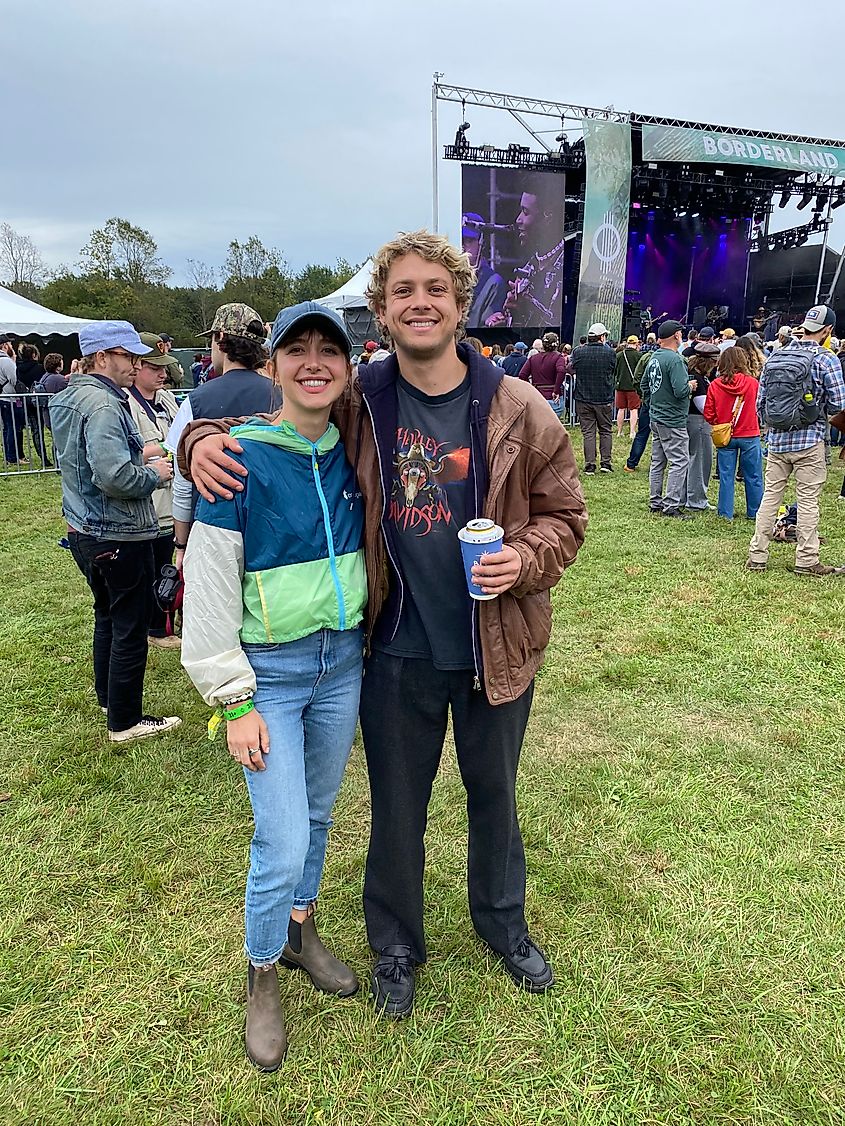 A couple poses in front of a modest music festival crowd.