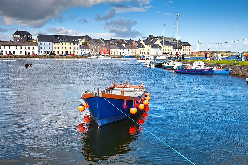 Boat in Galway Bay in front of old Galway and its pastel buildings.
