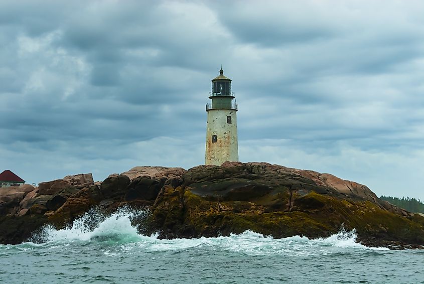 Peak lighthouse tower on a rocky island, on a cloudy day as the sun breaks through storm clouds in Maine