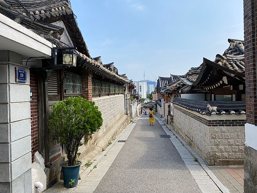 A woman in a yellow dress walks a small side street through a modernized hanok village.