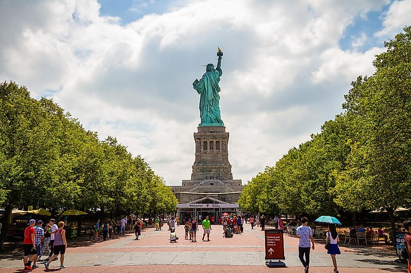  Tourists walking around the entrance of the Statue of Liberty behind the statue