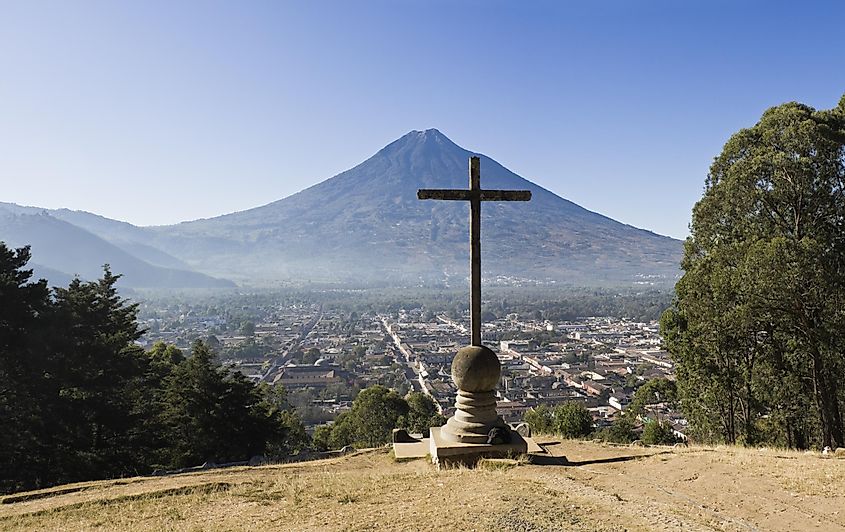 A hilltop cross overlooks a small colonial town and a massive volcano in the distance