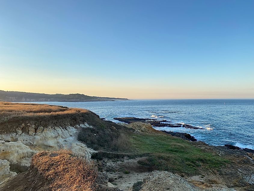 The first glimmers of the morning sun rising over grassy oceanfront cliffs.