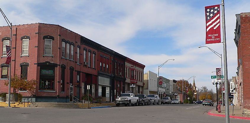Small-town street with historic red-brick buildings, American flags on lamp posts, and parked cars. A welcoming atmosphere with clear blue skies.