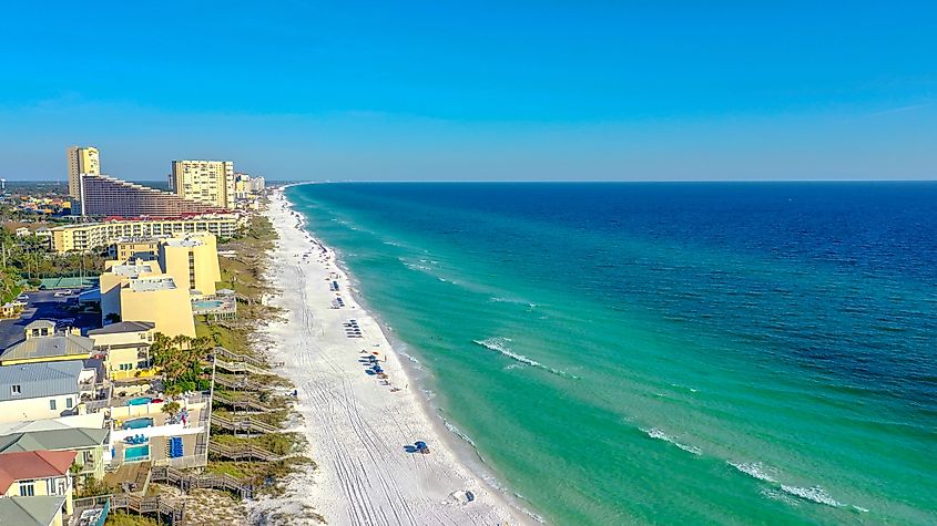 Aerial view of Miramar Beach, Florida, showcasing turquoise waters, pristine white sands, and coastal buildings under a clear blue sky.