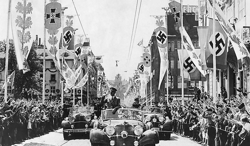 Adolf Hitler waving to crowds from his car at the head of a parade.