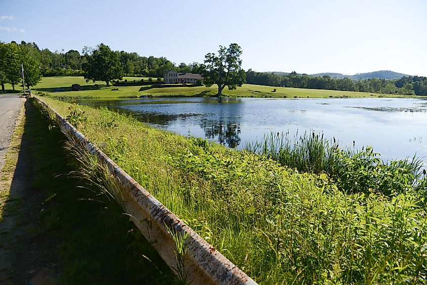 Scenic landscape of a pond and house viewed from a road's guardrail in Sturbridge, Massachusetts.