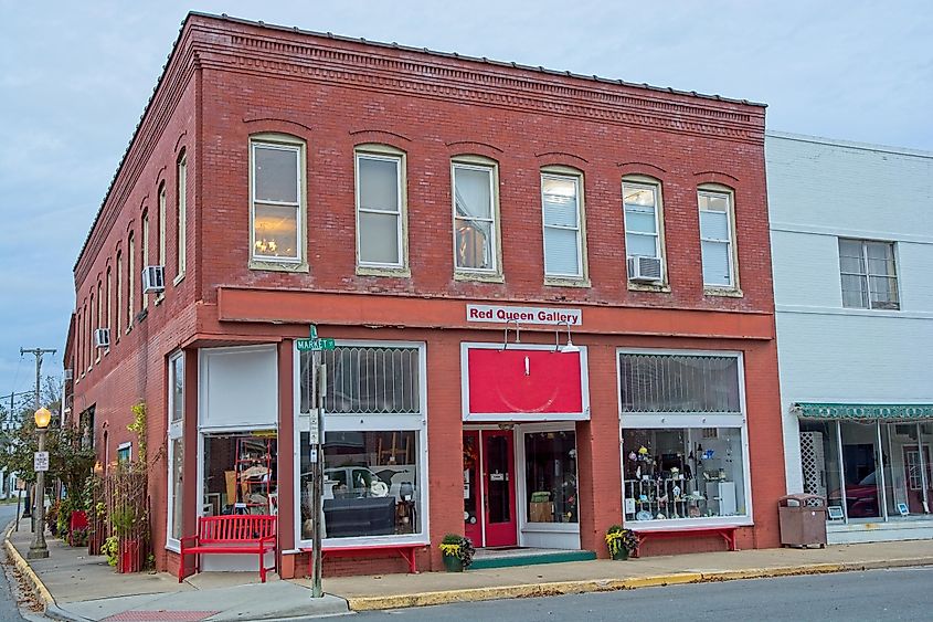 Onancock VA, USA — November 15, 2022: Red brick early 20th century store front on Market street housing the Red Queen Gallery in early evening light. Featuring works of art. Red bench on sidewalk.