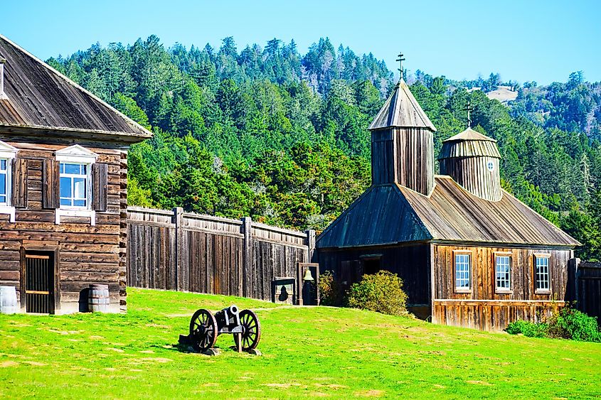 Scenic view of historic Fort Ross in California, wooden architecture, a chapel, and a cannon against a natural landscape of Sonoma County