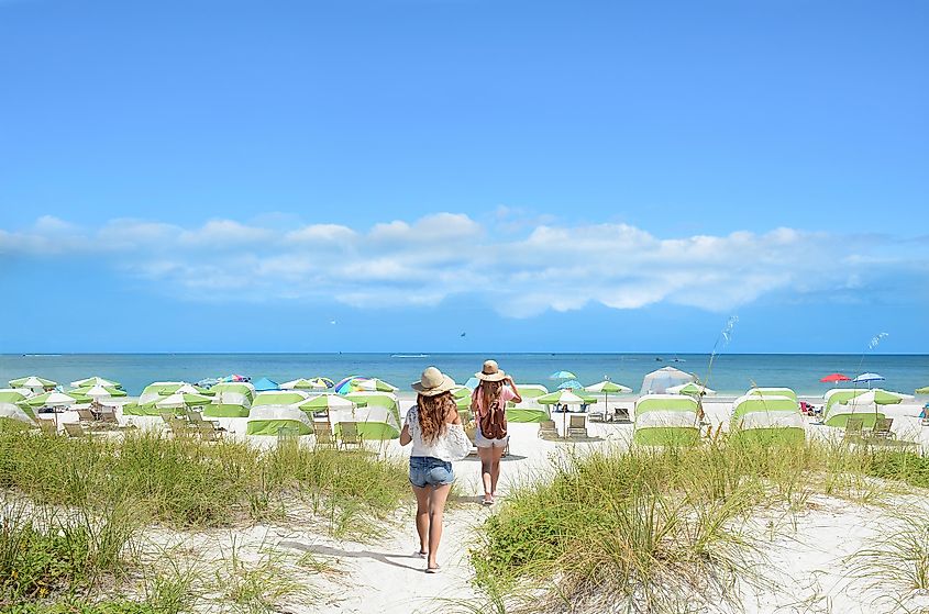 Girls walking on the beach on summer vacation. Beach chairs and parasols on beautiful white sand in the background. Gulf of Mexico, Clearwater Beach, Florida, USA.