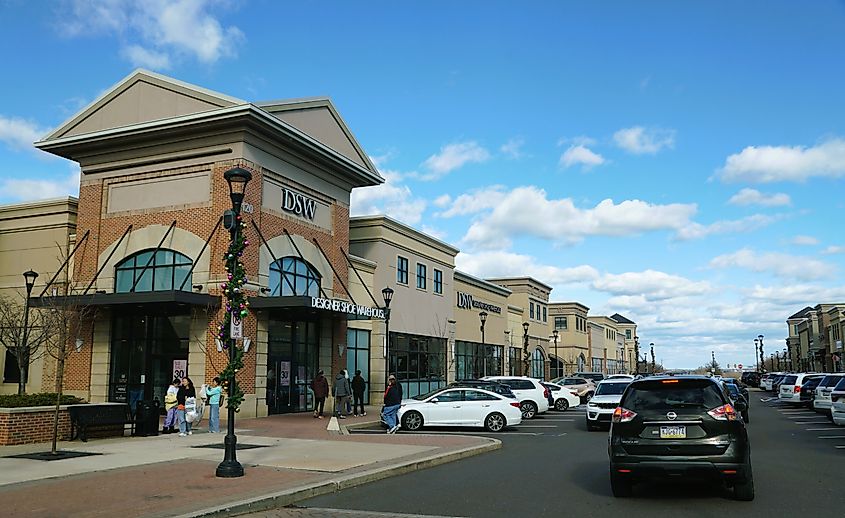 Designer Shoe Warehouse storefront in a busy retail plaza in Collegeville, Pennsylvania, with festive streetlamps and pedestrian activity