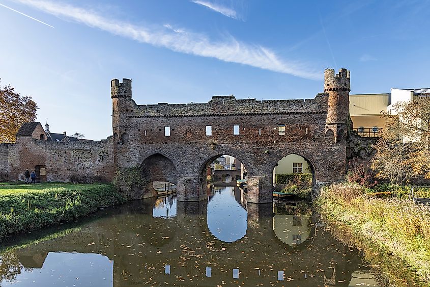 Medieval Berkelpoort water gate spanning the Berkel river with clear reflections and autumn colors in the historic city of Zutphen, Netherlands.