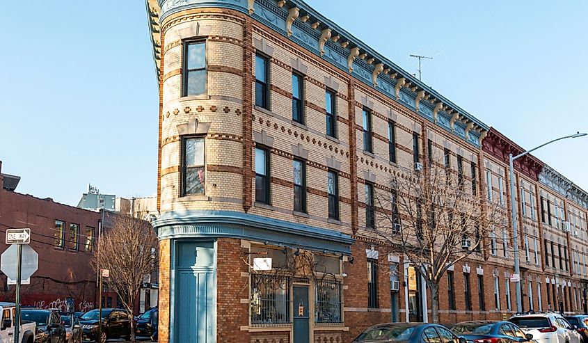 A triangular brick flatiron building with blue doors, trim and molding in a street corner in Astoria Queens New York City.
