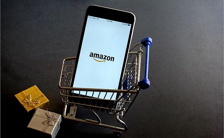 A phone displaying the Amazon app sits in a miniature shopping cart.
