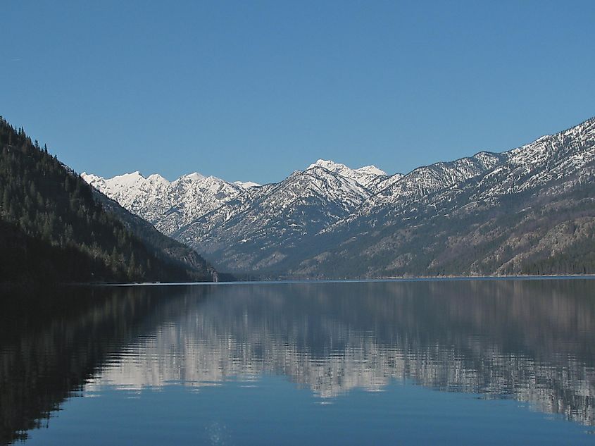 A pristine lake nestled amidst the rugged and remote Cascade Range in Washington, its clear waters reflecting the jagged, snow-capped peaks that surround it.