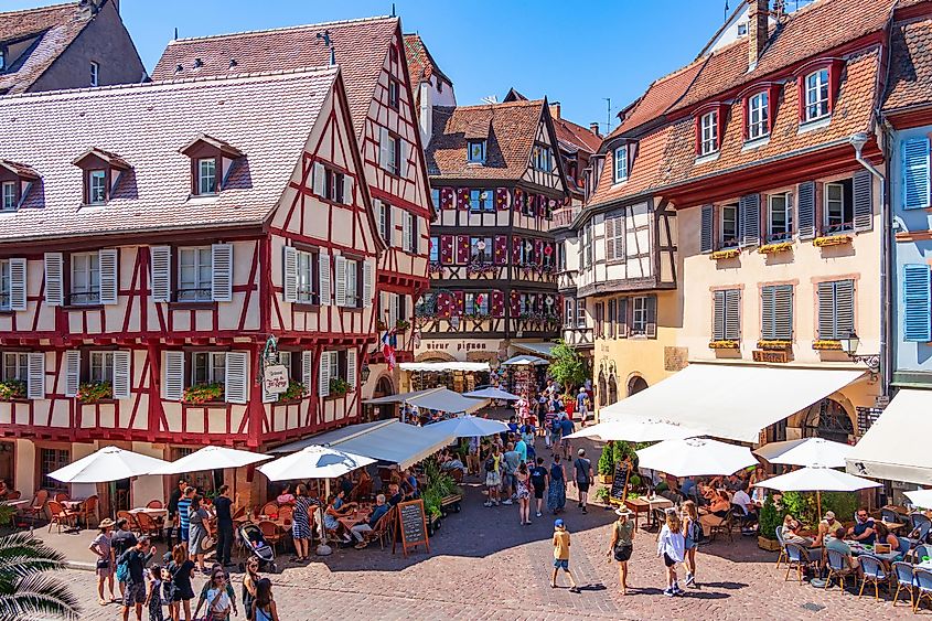 People relax in a summer cafe in the old town square with bright colorful facades of traditional fairy houses in Colmar