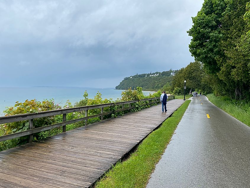 A man walks a waterside boardwalk next to a paved cycling path and the waters of Lake Huron.