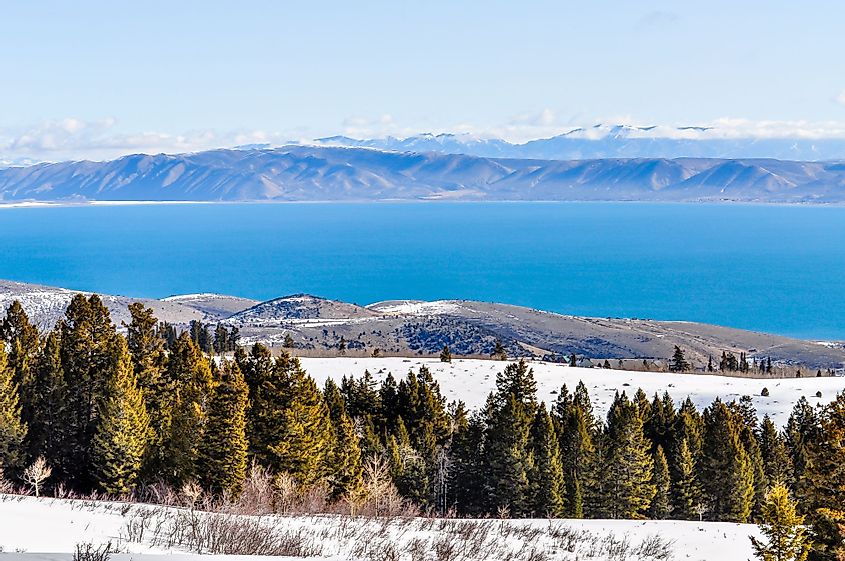 Trees and snow stand high above the blue waters of Bear Lake in Utah