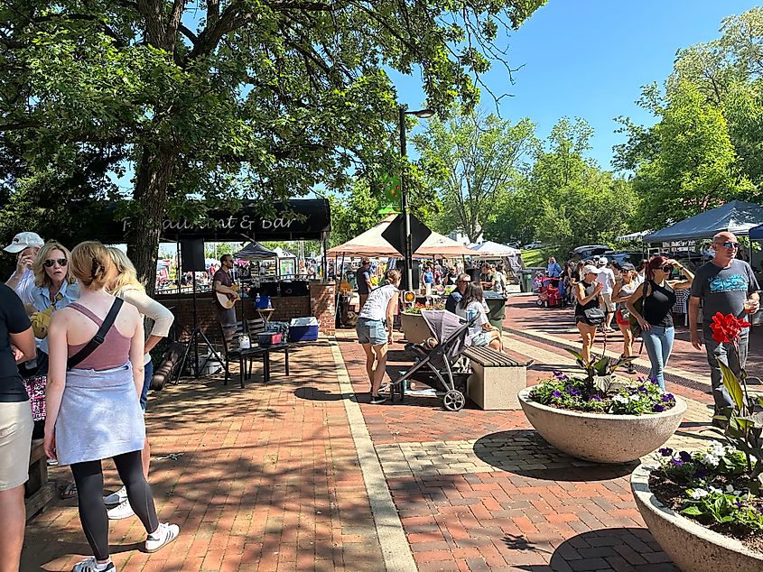 A large community gathering with live music taking place on a red-brick-lined pedestrian street.