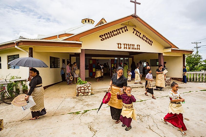 Polynesian parishioners in traditional Tongan dress walk out of church Sangata Teleisia 'o 'Avila as Catholic Mass ends, Pangai village, Ha'apai Group in Tonga, Polynesia, via maloff / Shutterstock.com
