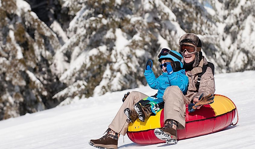 Young woman and child sliding down in inflatable snow tube