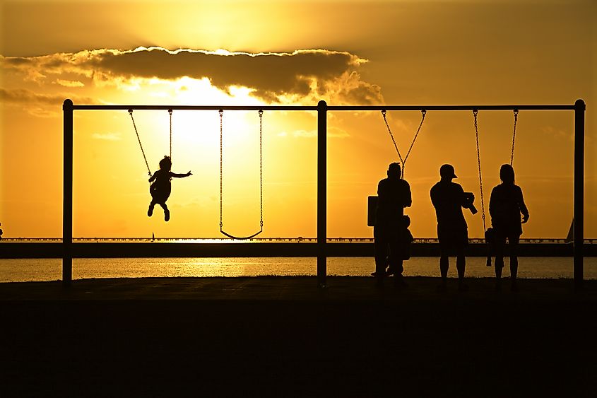 Mandeville, Louisiana: Families in silhouette play on the swings overlooking Lake Pontchartrain at sunset.