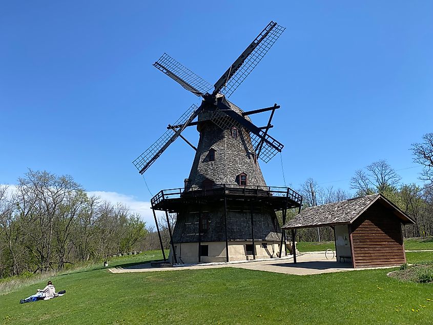 A couple lays in the grass next to a large Dutch windmill.