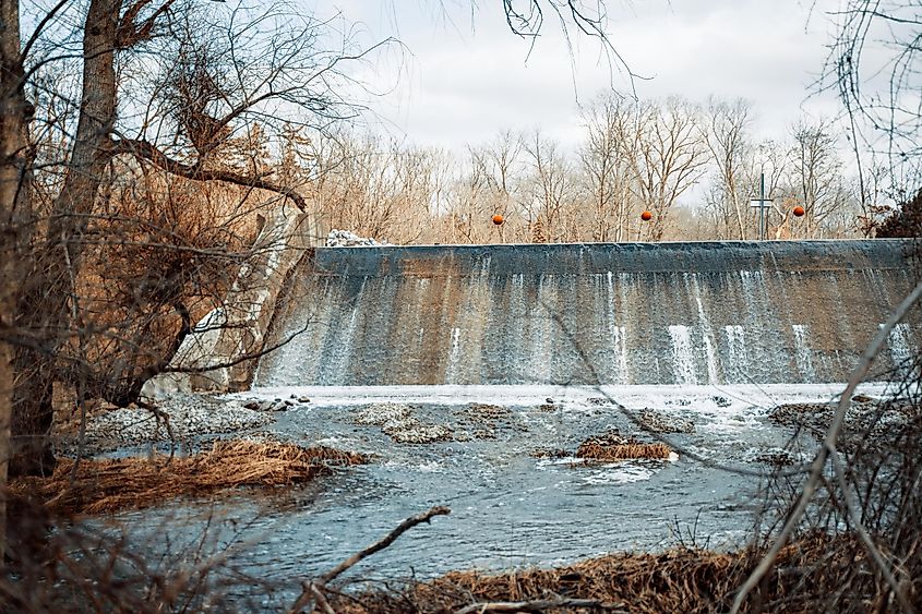 A beautiful view of a waterfall and leafless tress against cloudy sky during daytime at Marshall Riverwalk, Marshall, Michigan, United States