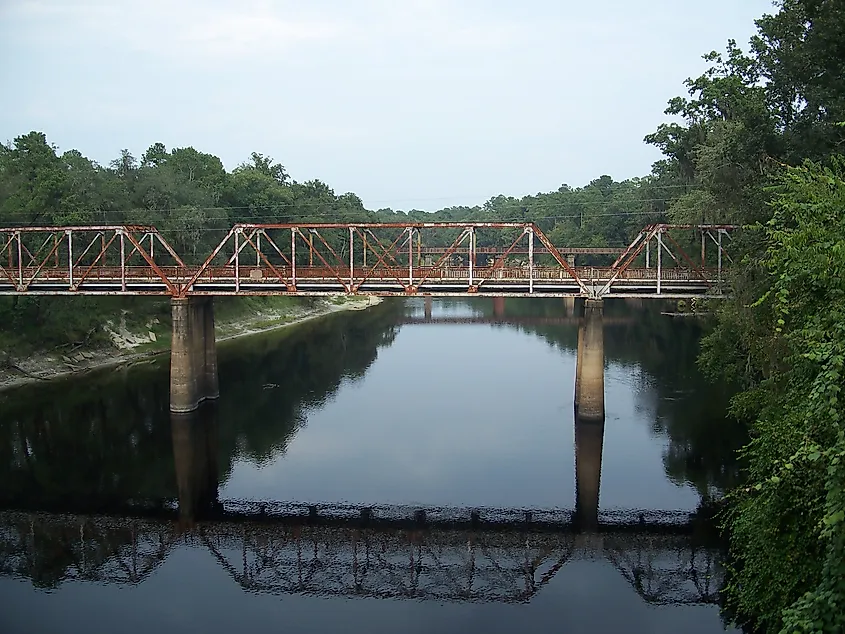 Suwanee River with the old steel truss US90 bridge reflected in it and a railroad bridge behind it.
