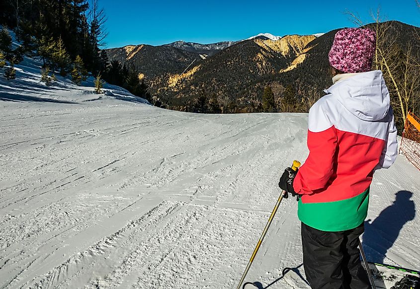 A woman skier with colorful clothing standing on Ski slope looking at Mountain View at Red River, New Mexico