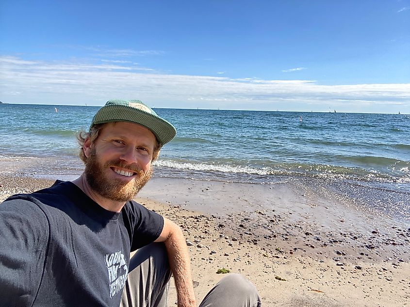 A man takes a smiling selfie on a sunny beach.