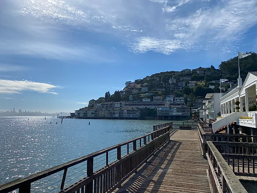 A waterfront boardwalk looks ahead to colorful homes on a verdant hill, and over to San Francisco's skyline.