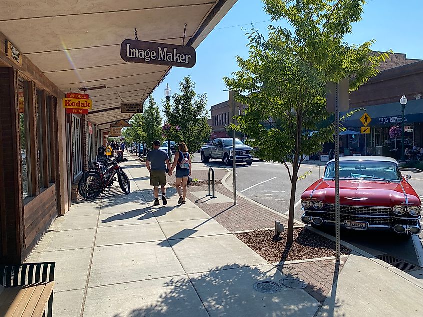 A couple walks past shops and a bright red old fashioned corvette on main street Sandpoint, ID