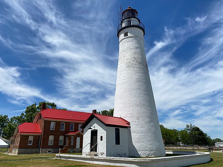 A large white lighthouse stands beside a red brick building with bright red roof.