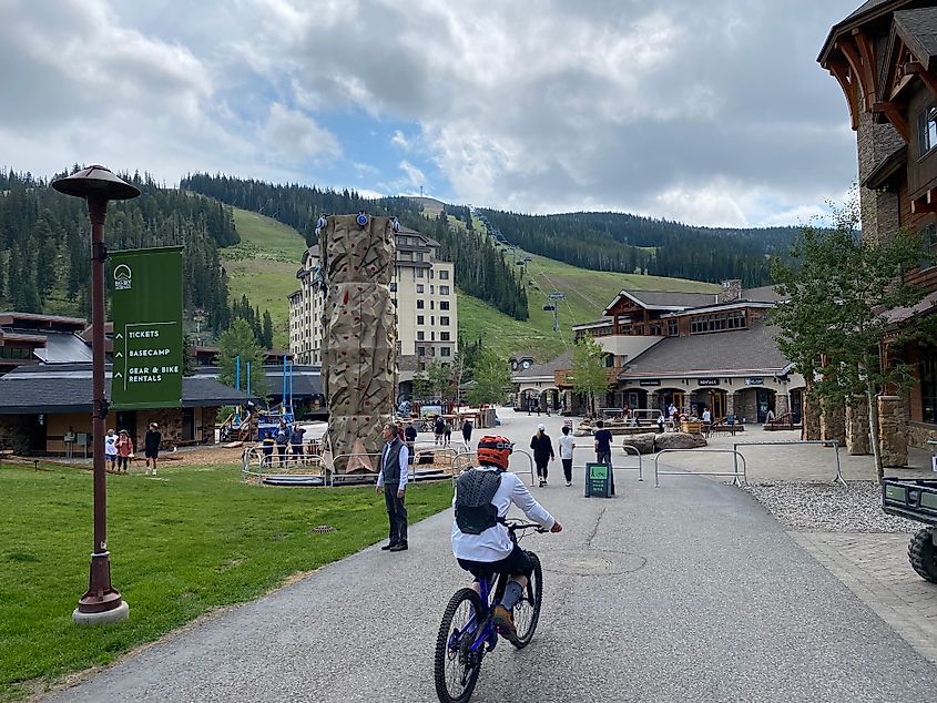 A mountain biker heads past an outdoor climbing wall, toward the snow-free slopes of Big Sky's Lone Mountain in the summer off-season.