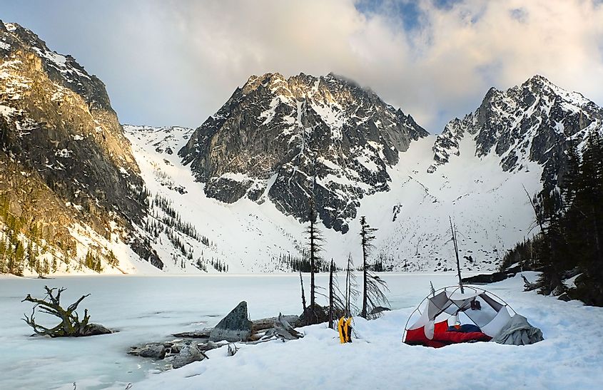 Sunset illuminates Colchuck and Dragontail Peaks over a frozen Colchuck Lake and a tent.