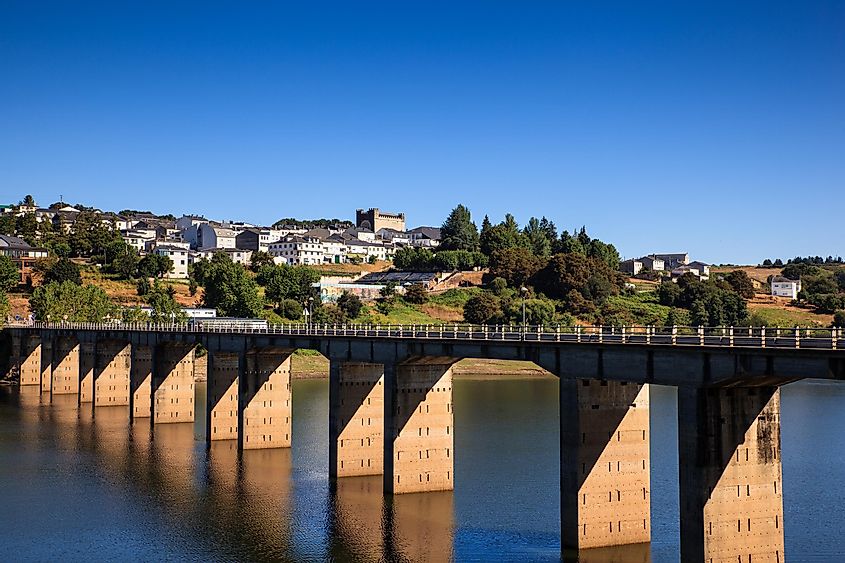 A long bridge with many arches crosses a wide river to get to a quaint hillside town
