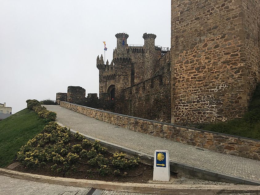 The Knights Templar Castle of Ponferrada, Spain. The typical yellow and blue marker of the Camino de Santiago stands in front. 