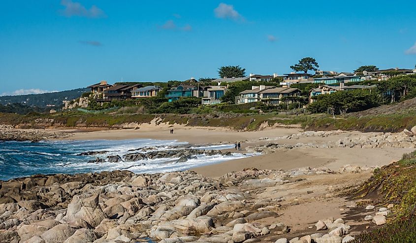 Waves break on the rocky pacific coast along the beach of central Coast of California, in Carmel by the Sea, with luxury houses on the adjacent hillside bluffs.