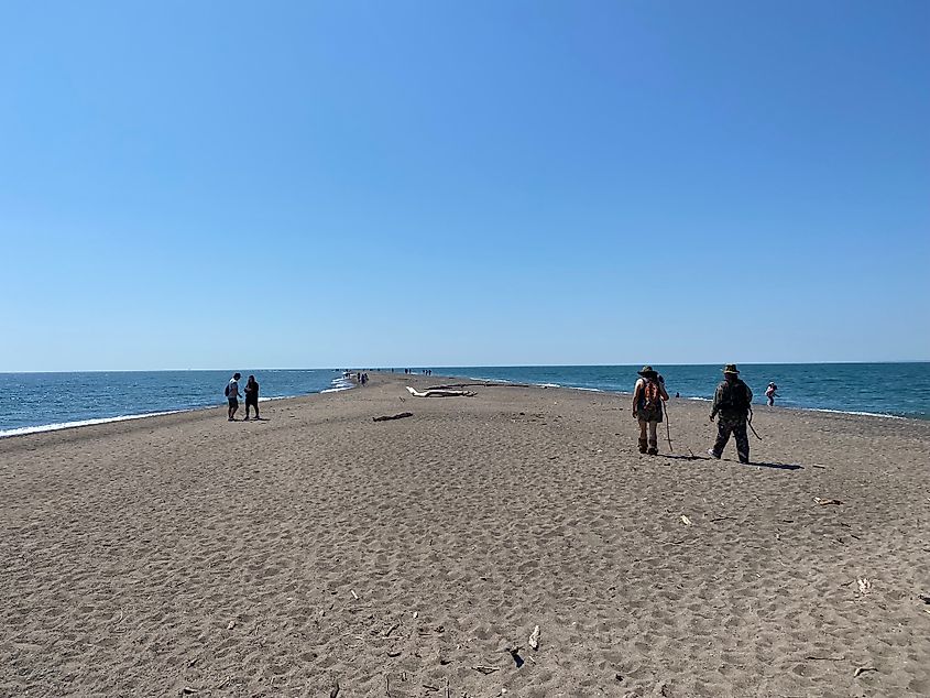 Disparate groups of people walk out to the tip of a long sand spit.