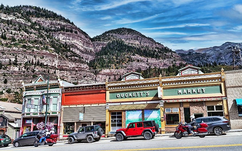The historic downtown Main street with parked car and passing motorcycles with San Juan mountains in background - Ouray, Colorado