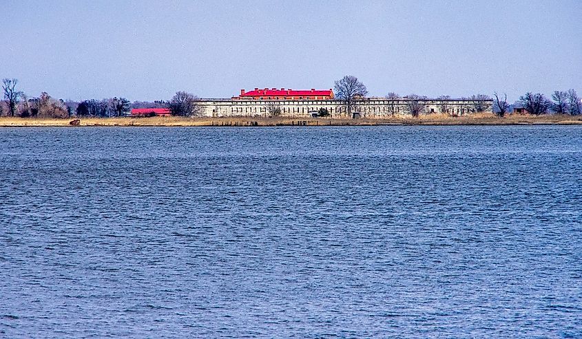 Pea Patch Island, Delaware, view of civil war era fortifications of Fort Delaware across the harbor from Delaware City with calm water and clear sky in mid-day.