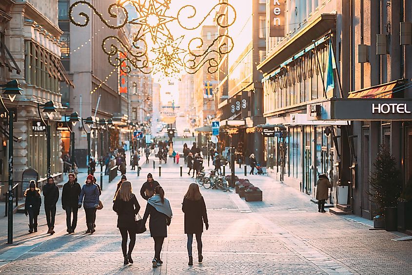 People Walking On Kluuvikatu Street In Winter Sunny Day. Street Decorated For Christmas And New Year Holidays