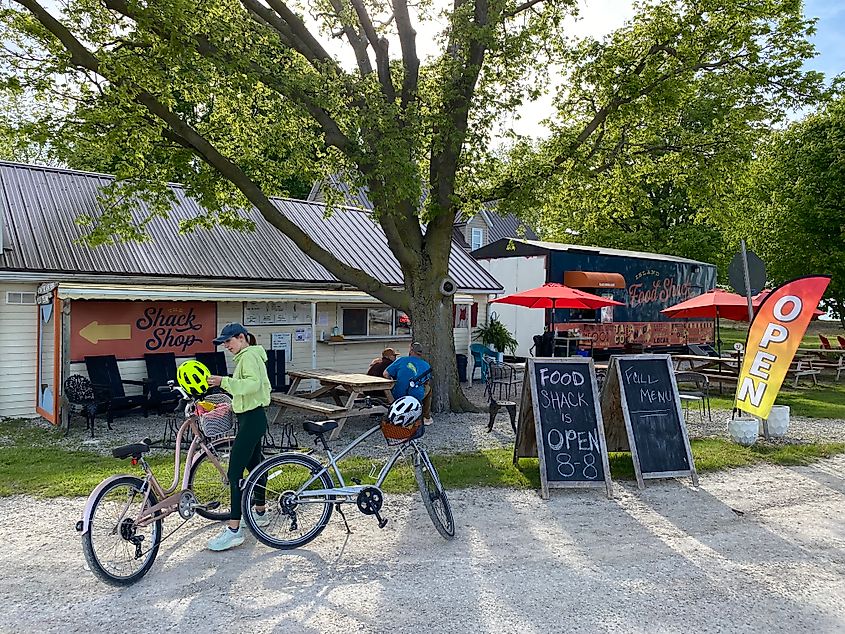 A woman parks her bike at a collection of small town food stalls with picnic tables on the grass out front.